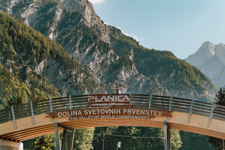 kolesar stoji na nadhodu z napisom Planica in drži kolo nad glavo